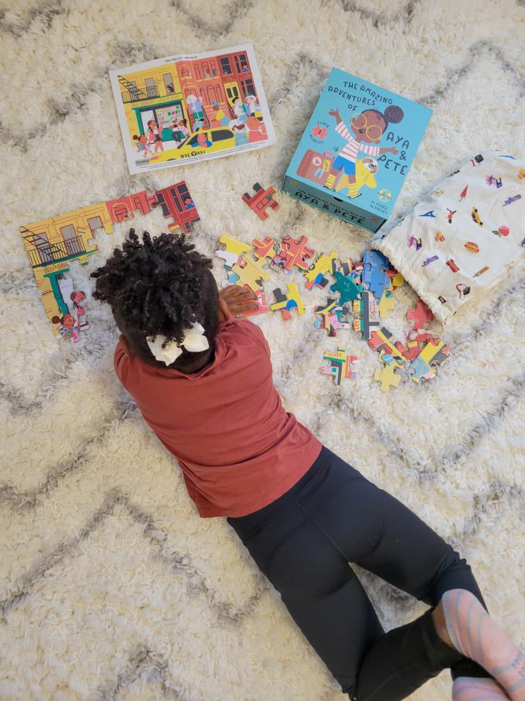 Picture shows a little girl with curly hair lying on a rug assembling an Aya & Pete children's puzzle. Puzzle pieces surround her.